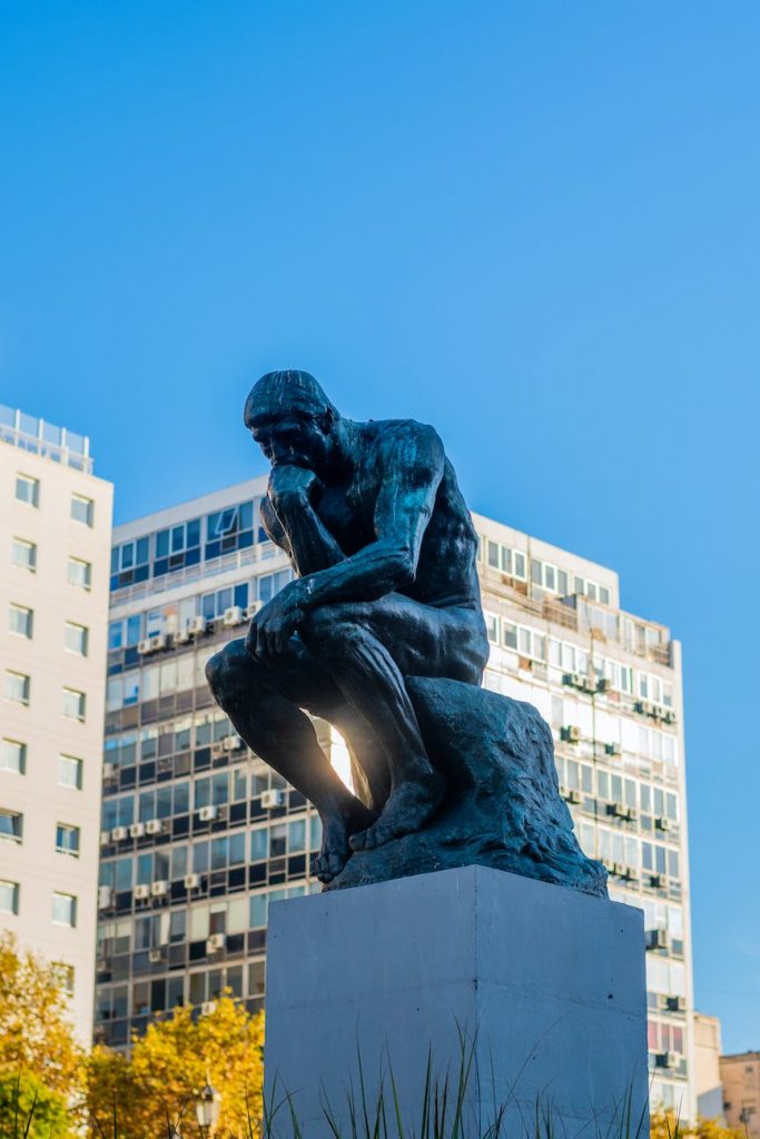 the thinker statue near buildings under blue sky